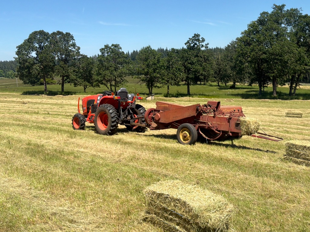 Orange Kubota tractor and red New Holland hay baler in an Oregon agricultural field with fresh hay bales